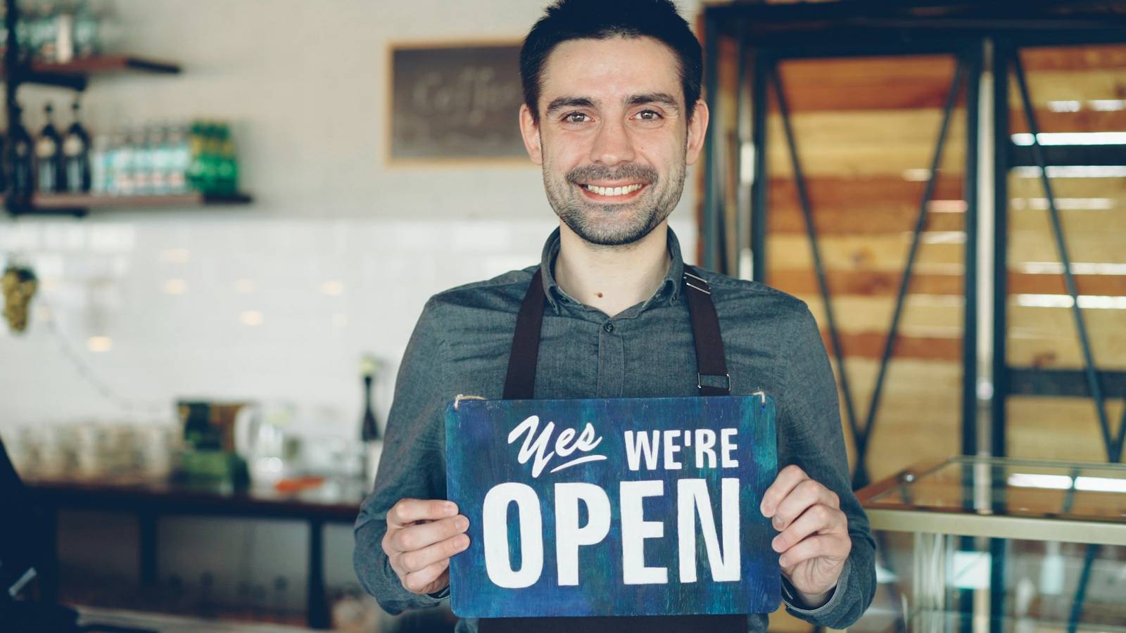 Lächelnder Ladeninhaber hält ein Schild «We're open»